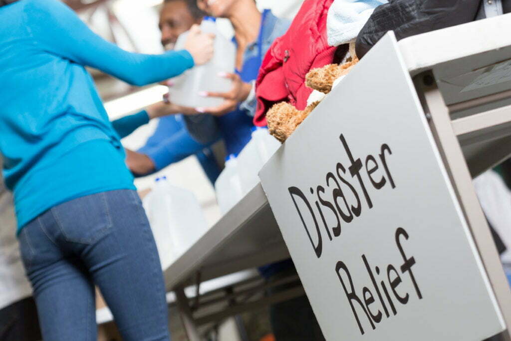 A women receives a jug of fresh water from workers behind a table at a disaster relief center. 