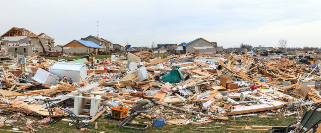 Damaged homes and debris from homes destroyed during a storm covers a field of grass where homes once stood.