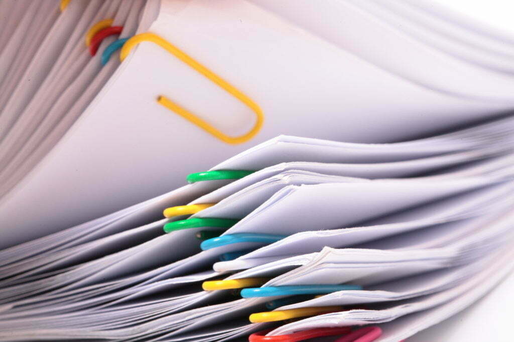 A stack of papers being flipped through, each paper is bound individually with colorful paper clips. 