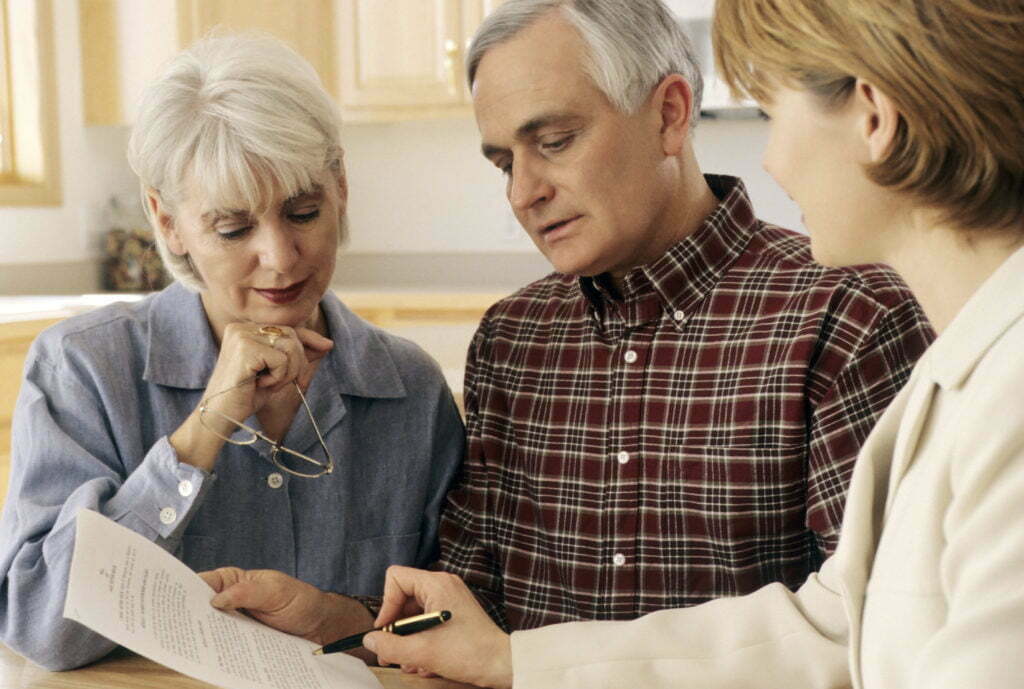 Senior couple looking at paperwork with case manager at home. 