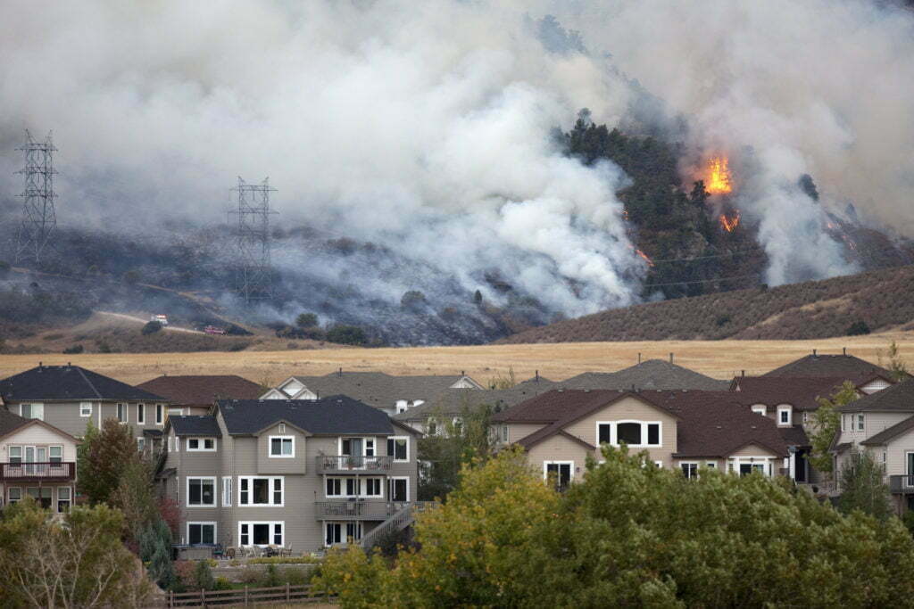 Pine trees and scrub oak burn behind homes.