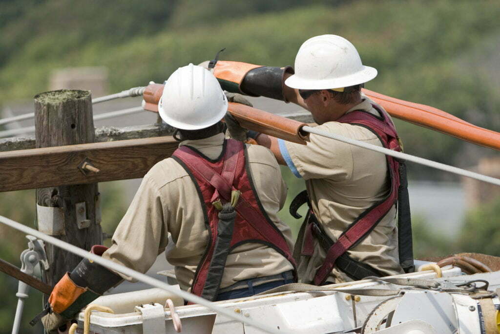Pole-level view of electric utility workers making repairs on transmission lines damaged in a severe wind storm.