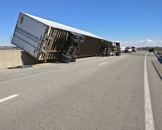An 18-wheeler tipped on its side in the middle of a highway.