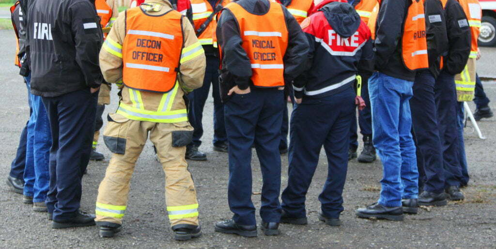 The backs of emergency responders huddled in a circle having a discussion. 