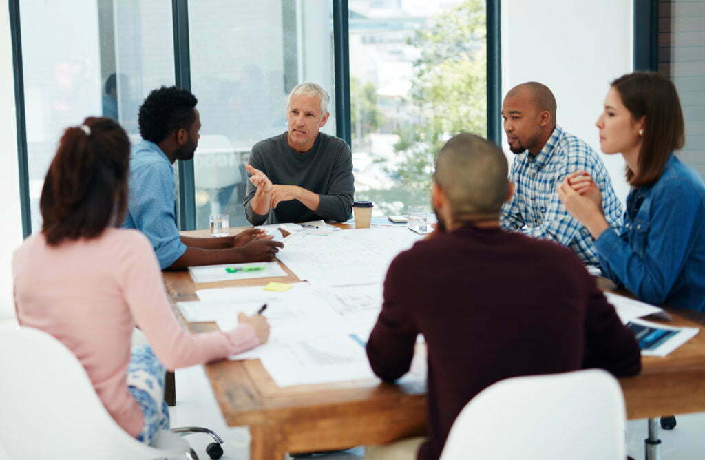 A diverse group of grant program managers and staff sit around an office table in a meeting.
